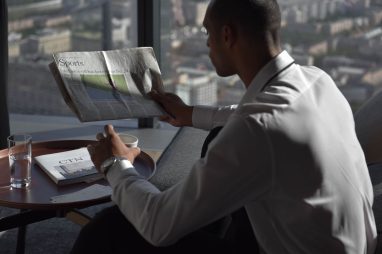 Businessman in office reading sports section, enjoying coffee with city view. — Roulettino Casino: Was macht diese Plattform
