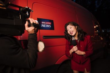 Asian female reporter in a red blazer reporting live on the news outdoors in the evening. — TonySpins Casino und seine innova