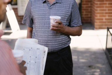 Crop anonymous ethnic male friends with coffee to go and newspaper speaking on city pavement — Wie fair sind die Spiele im Lo