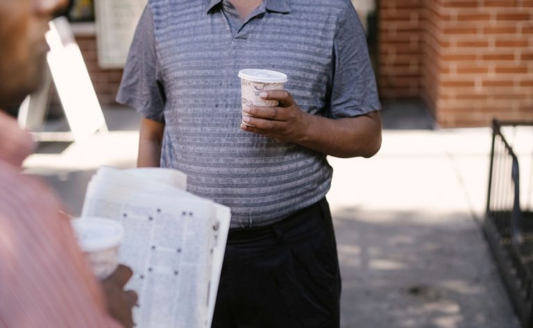 Crop anonymous ethnic male friends with coffee to go and newspaper speaking on city pavement — Wie fair sind die Spiele im Lo