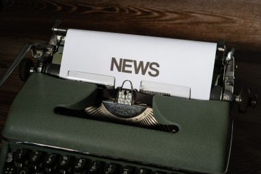 A retro typewriter featuring a 'NEWS' headline typed on white paper against a wooden surface. — Wie gut sind die Support-Opti
